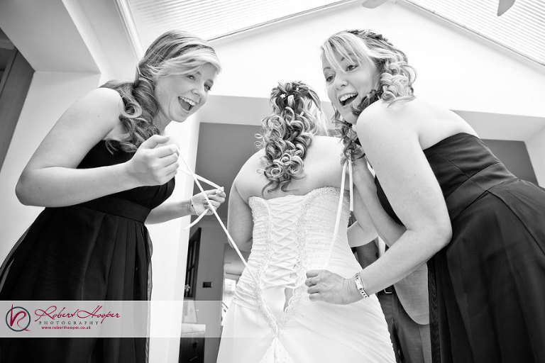 Bridesmaids lacing up bride's wedding dress 