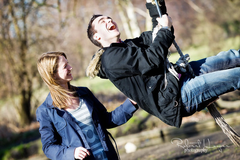 Laughing couple on rope swing in park 