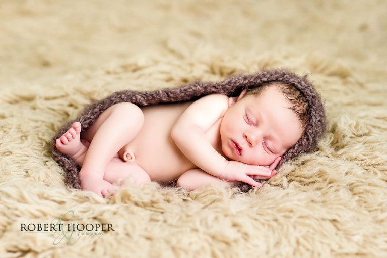 Sleeping newborn baby in cocoon on shaggy rug