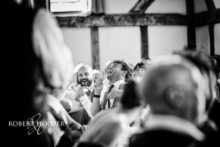 Bridesmen laughing hilariously during wedding breakfast speeches at Tithe Barn wedding venue, Loseley Park, Surrey