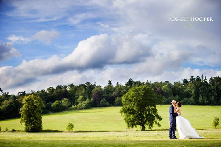 Surrey bride and bride groom kissing in landscape shot with dramatic sky at Loseley Park wedding venue near Guildford