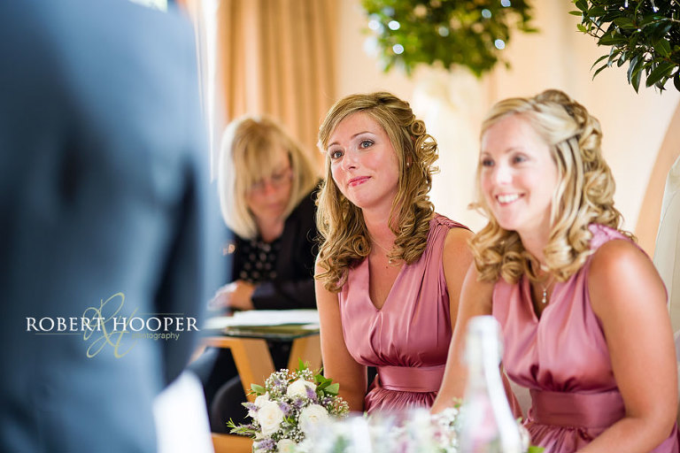 Bridesmaid in pink salmon pink dress gazing at bride and groom during wedding vows at Cain Manor in Surrey