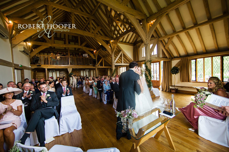 Bride and groom kiss after vows and guests clap at Cain Manor wedding venue in Surrey