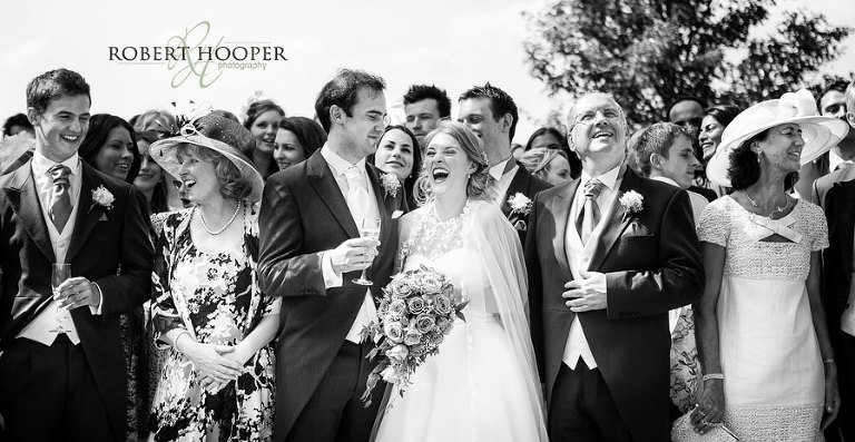 Black and white photograph of bride and guests laughing after group shot at Cain Manor Surrey