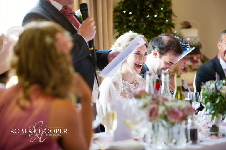 Bride and groom laughing at father-of-the-bride's speech during wedding breakfast at Cain Manor in Surrey