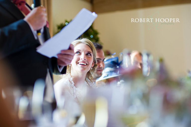 Bride smiling lovingly at her groom on the top table at wedding breakfast at Cain Manor Surrey