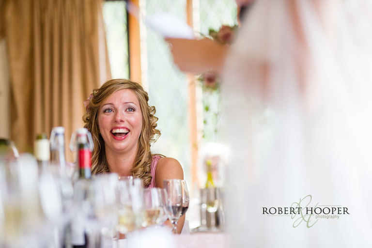 Bridesmaid laughing at bride's speech on top table at wedding breakfast at Cain Manor in Surrey