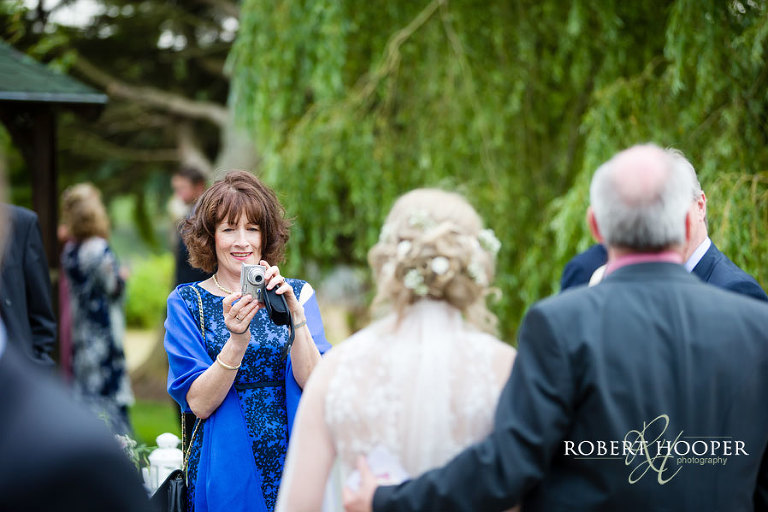 Wedding guest taking photography of bride and bride's father at Cain Manor near Grayshott in Surrey