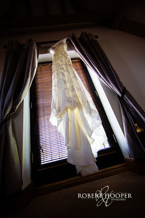 Beautiful wedding dress hanging in window during bridal preps at Cooling Castle Barn in Rochester, Kent