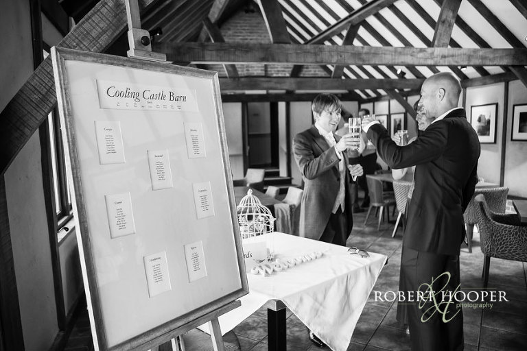 Wedding table plan and groom welcoming guests to Cooling Castle Barn wedding venue in Rochester, Kent