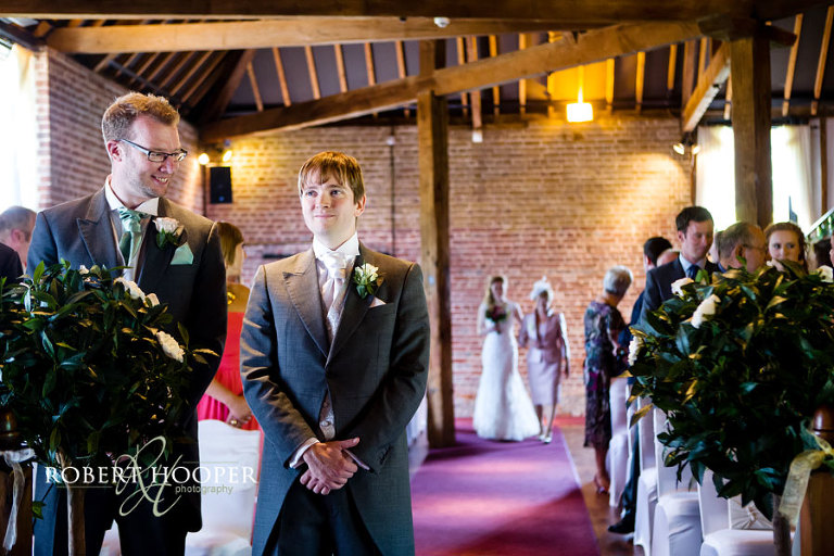 Bride walking down the isle with groom waiting pensively at the alter at summer wedding in Cooling Castle Barn, Rochester in Kent
