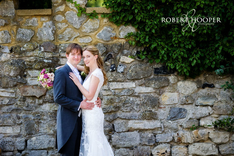 Bride and groom in an embrace in front of stone wall at Cooling Castle Barn in Rochester, Kent