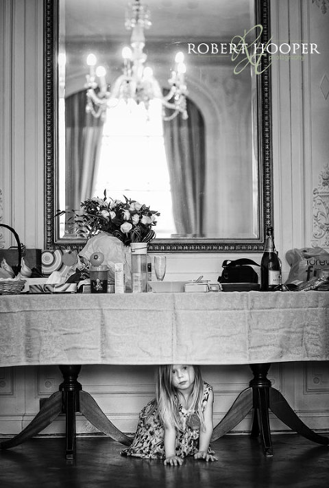 Flower girl peeping out from under the table during bride preparations at Addington Palace, Surrey