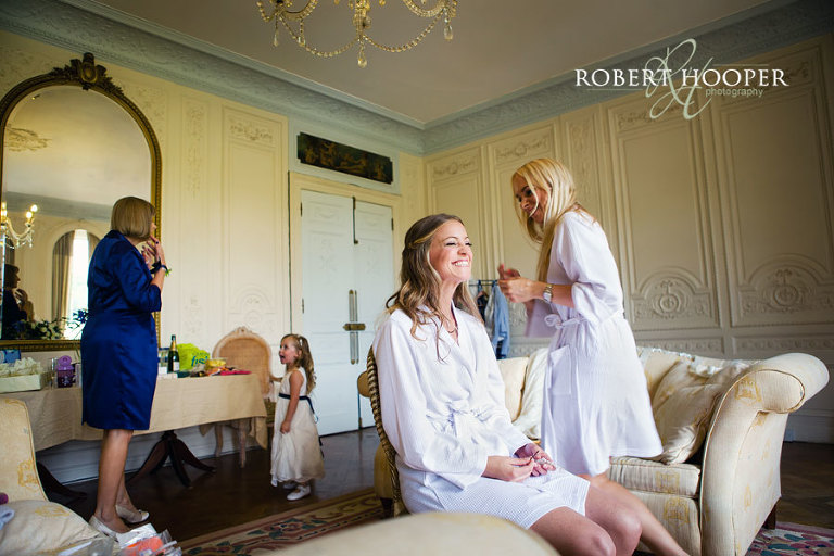 Bridal and bridesmaid giggling during make-up preparations for summer wedding at Addington Palace, Surrey