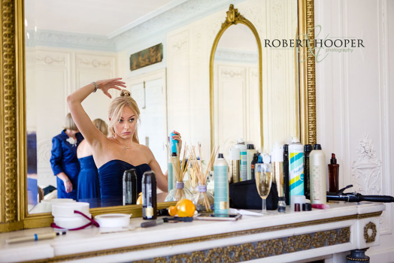 Bridesmaid in blue dress looking in the mirror, doing her hair during bridal preps at Addington Palace in Surrey