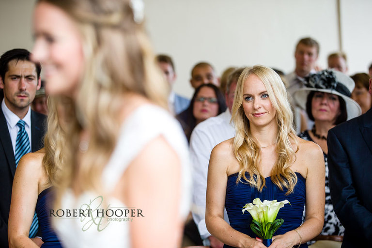 A tender look from a bridesmaid to the bride and bride groom during their wedding vows in the Winter Garden Room at Addington Palace in Croydon Surrey