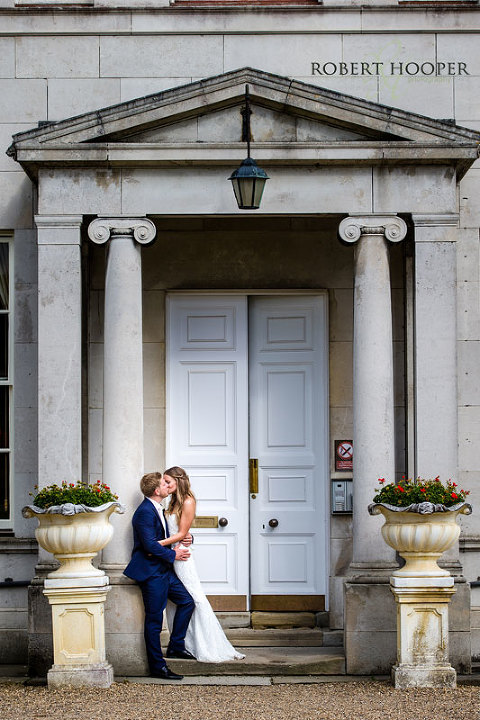 Bride and bride groom embracing in front of the big white doors of Addington Palace wedding venue in Croydon, Surrey