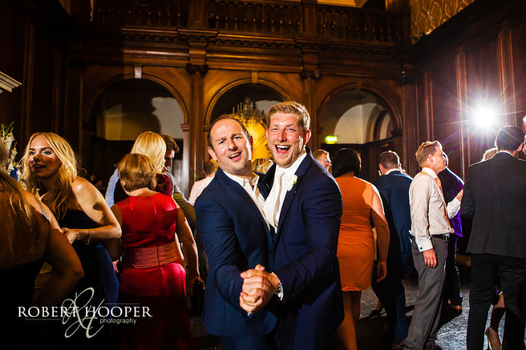 Groom and guest in dance hold and singing to the band in the Great Hall at Addington Palace in Surrey