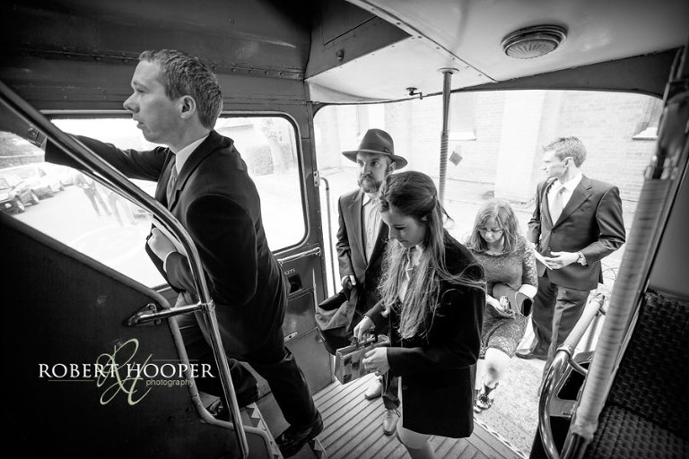 Wedding guests boarding a red bus to transport them from St Andrew the Apostle Parish Church in Catford to Addington Palace in Surrey for wedding drinks and canapes reception