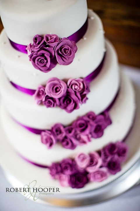 Four tier wedding cake decorated with purple flowers for wedding reception in The Great Hall at Addington Palace in Surrey
