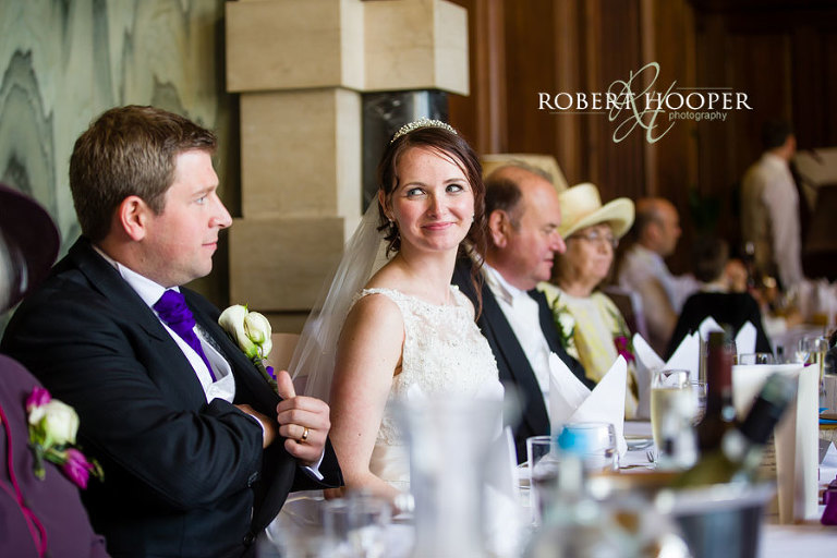 Bride glancing at Groom before his speech in the Great Hall at Addington Palace in Surrey