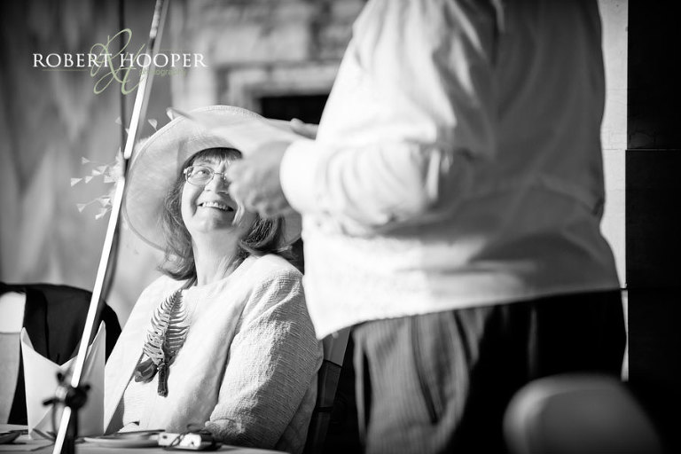 Black and white photo of bride's mum enjoying groom's speech during wedding breakfast in the Great Hall, Addington Palace in Surrey