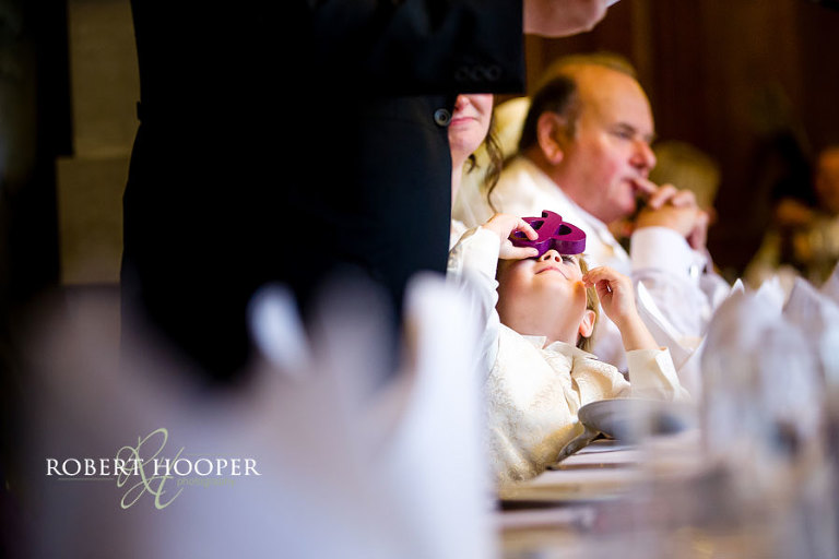 Page boy sitting at top table during groom speech in the Great Hall at Addington Palace, Surrey