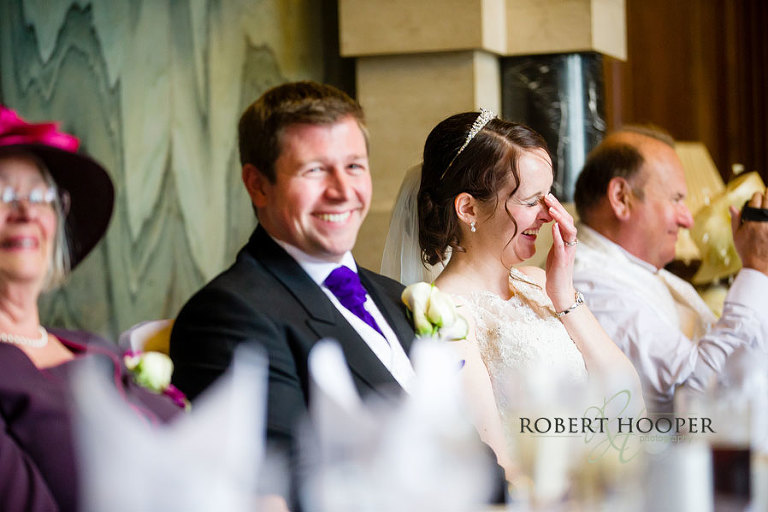 Bride and groom on top table laughing at speeches during wedding breakfast in The Great Hall, Addington Palace, Surrey