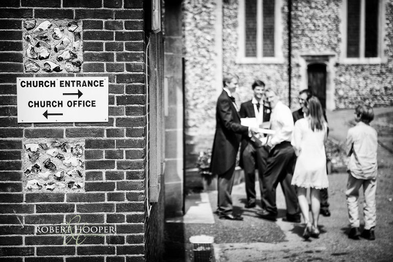 Creative documentary style image of groomsmen on wedding day welcoming guests to All Saints Church, Orpington, Kent