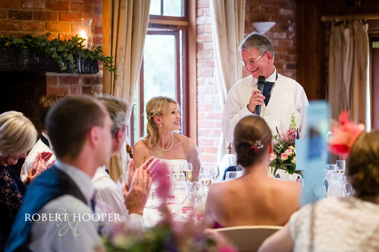 Natural photograph of bride laughing during dad's speech at wedding breakfast, Westerham Golf Club in Kent