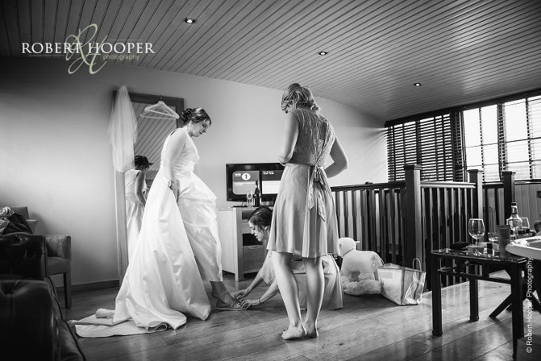 Bridesmaid helping bride put on comfortable shoes for wedding ceremony at Bix Manor, Henley on Thames in Oxfordshire