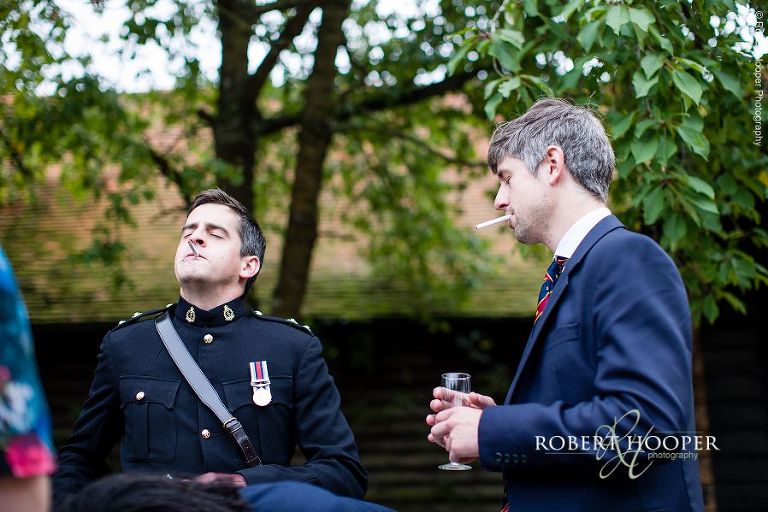 Guests enjoying a cigarette at wedding drinks reception in courtyard at Bix Manor, Henley-on-Thames, Oxfordshire