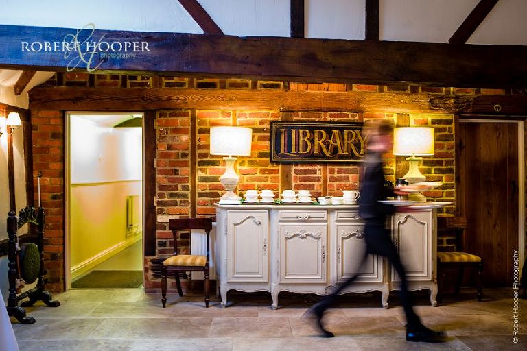 Waiter rushing through library to serve guests at wedding breakfast in Great Tithe Barn, Bix Manor, Henley-on-Thames, Oxfordshire