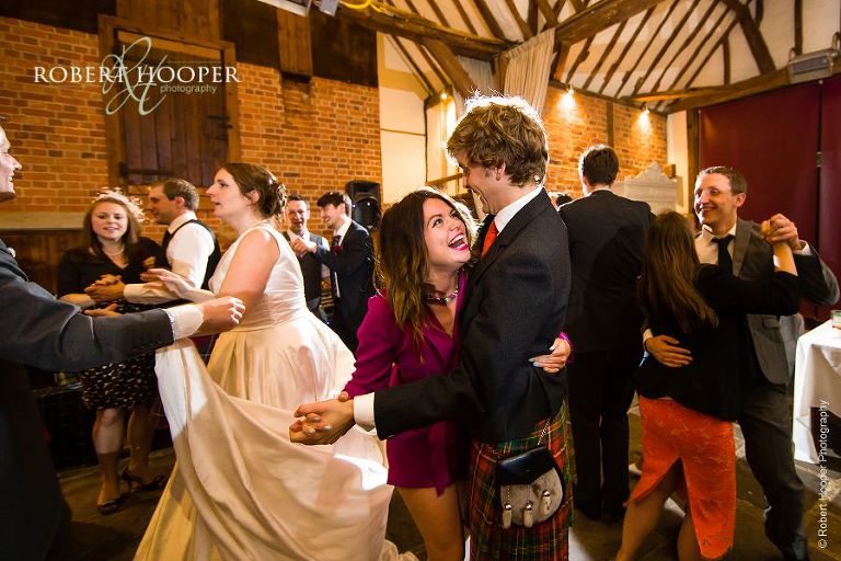 Bride and groom and wedding guests in their kilts Ceilidh dancing at wedding celebration at Bix Manor Oxfordshire