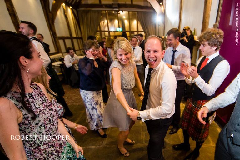 Wedding guests having fun Ceilidh dancing at evening reception in Great Tithe Barn, Bix Manor in Oxfordshire