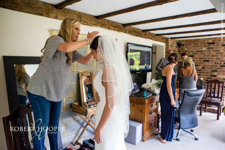 Bride having her veil put on by hairdresser during bridal preps on wedding day in Send, Surrey