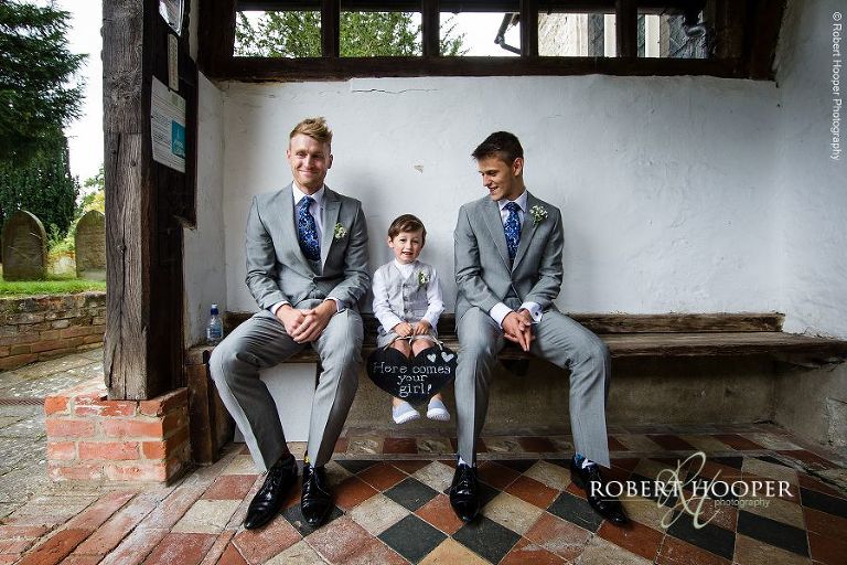 Groomsmen and page boy waiting at the entrance to the church for the bride's arrival on summer wedding day in Send, Surrey