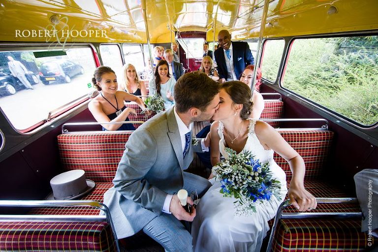 Bride and bride groom kiss aboard their Red London bus outside Send Church in Surrey