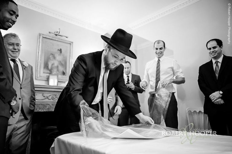 Rabbi removing Torah portion from protective cover for tish at Jewish wedding ceremony at Northbrook Park in Surrey