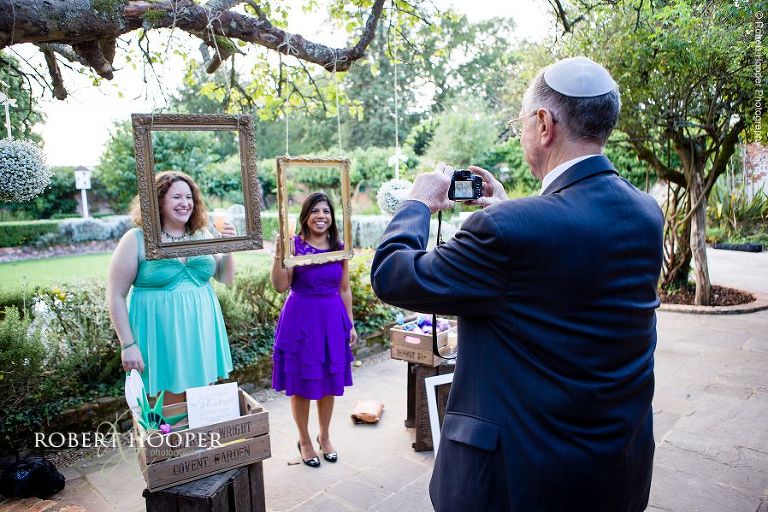 Wedding guests taking pictures of each other using hanging frames in gardens at Northbrook Park wedding venue in Surrey