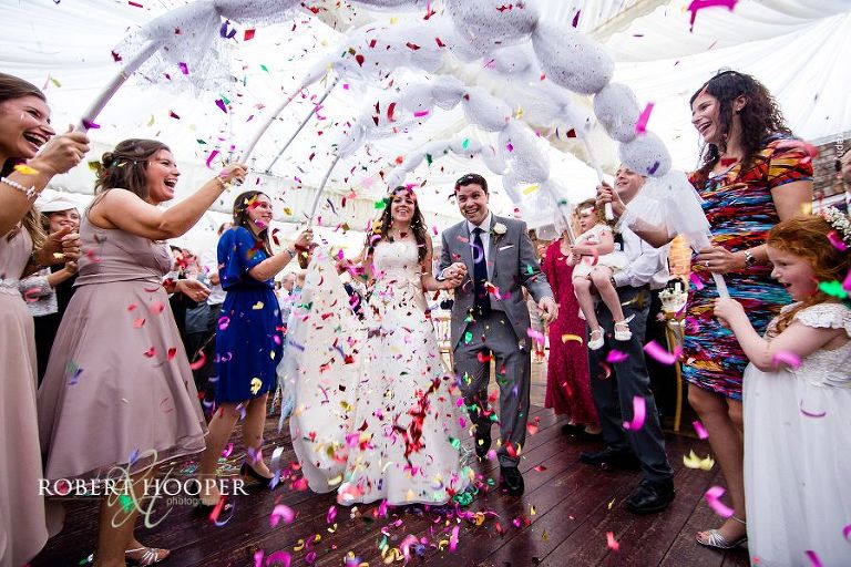 Bride and groom's entrance to wedding feast (Mitzvah) and guests celebrating with giant confetti crackers at Nprthbrook Park in Surrey