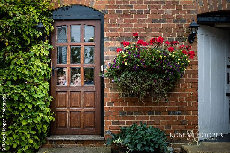 Flower girl and page boy peeking out the door on wedding day at Coltsford Mill, Oxted in Surrey