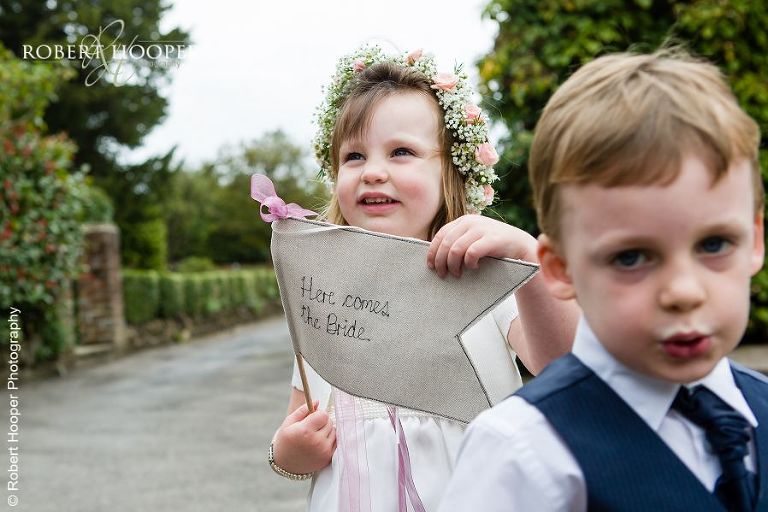 Flower girl holding her "here comes the bride" flag on wedding day at Coltsford Mill, Oxted in Surrey