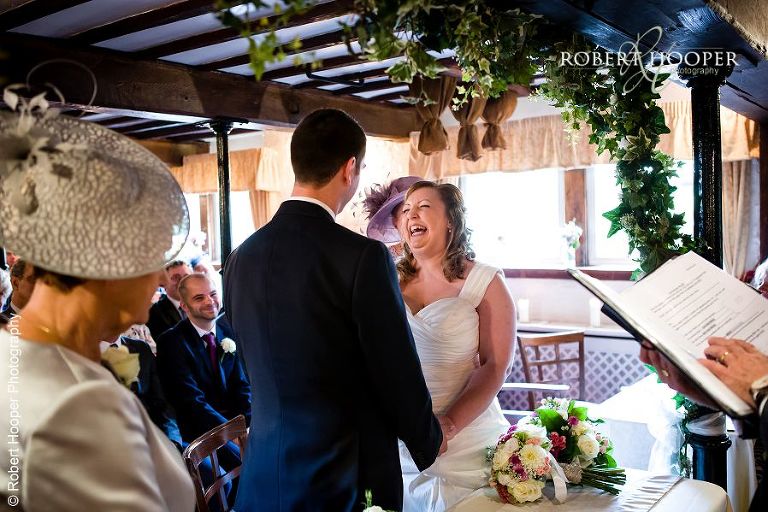 Bride and groom sharing laughter during their civil wedding ceremony at Coltsford Mill, Oxted in Surrey