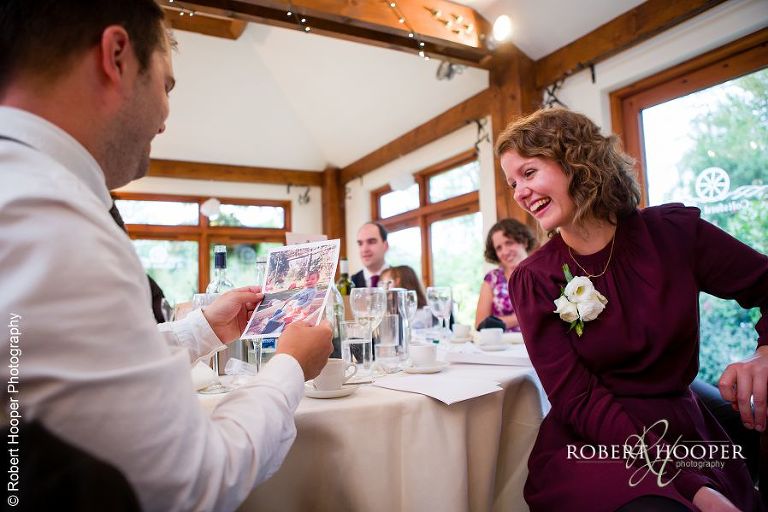 Wedding guests looking at pictures of groom handed out during best man's speech at Coltsford Mill, Oxted in Surrey