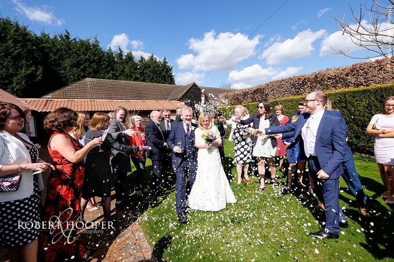 Wedding guests throwing confetti over bride and groom after their civil ceremony at Oaks Farm Barn in Surrey