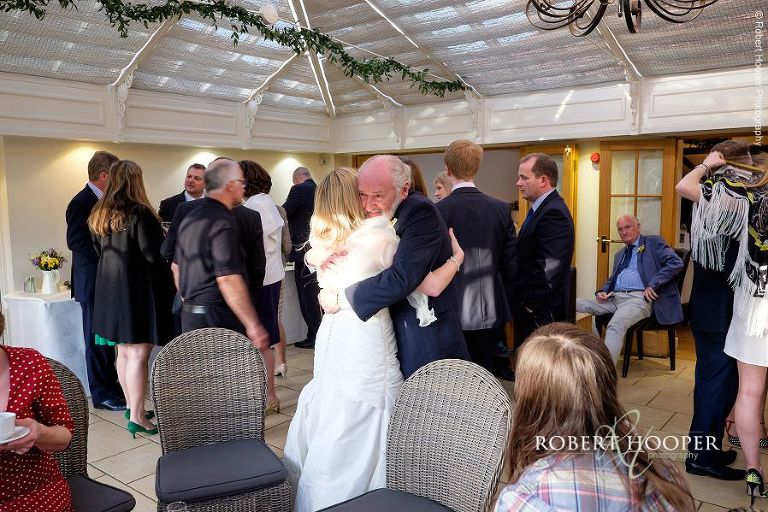 Bride hugs her father-in-law at on her wedding day at Oaks Farm Barn in Surrey