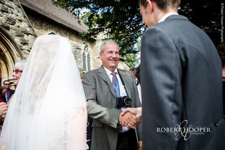 Wedding guests congratulate bride and groom following their wedding ceremony at St Peter and St Paul's Church in Aylesford, Kent