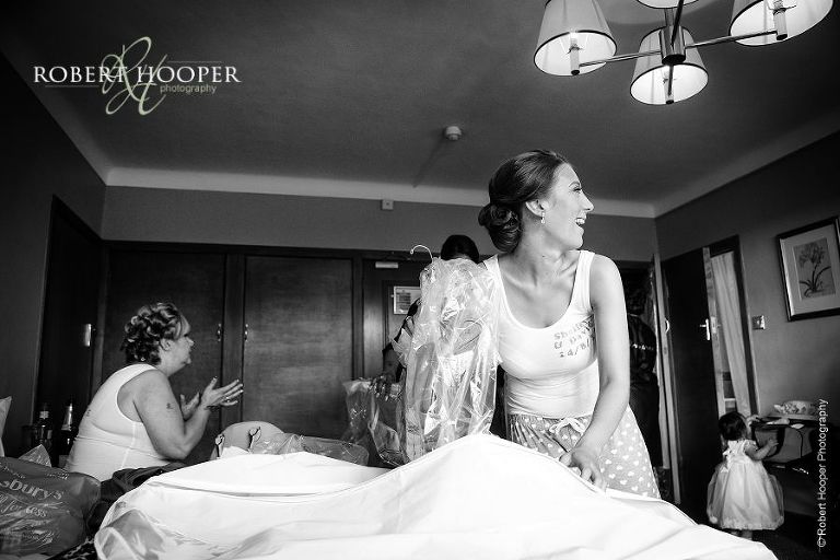 Bridesmaid taking wedding dress out of its bag to hang up on wedding day during bridal preps at Selsdon Park Hotel in Croydon, Surrey
