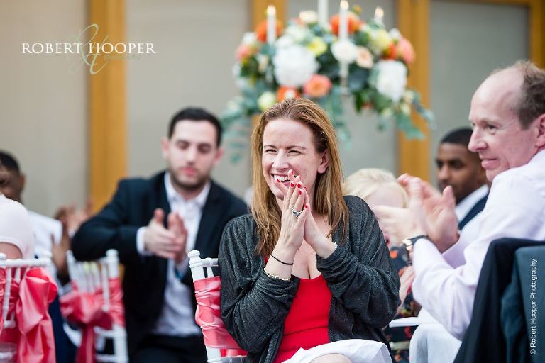 Guests laughing at father of the bride's speech at wedding breakfast in the glass atrium at Botleys Mansion in Surrey